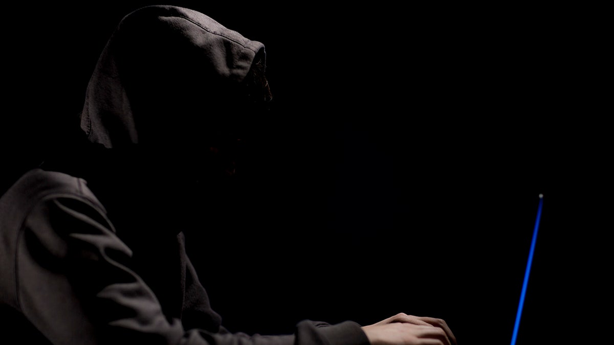 An Illustration of a man wearing a hoodie looking at a laptop in a black background.