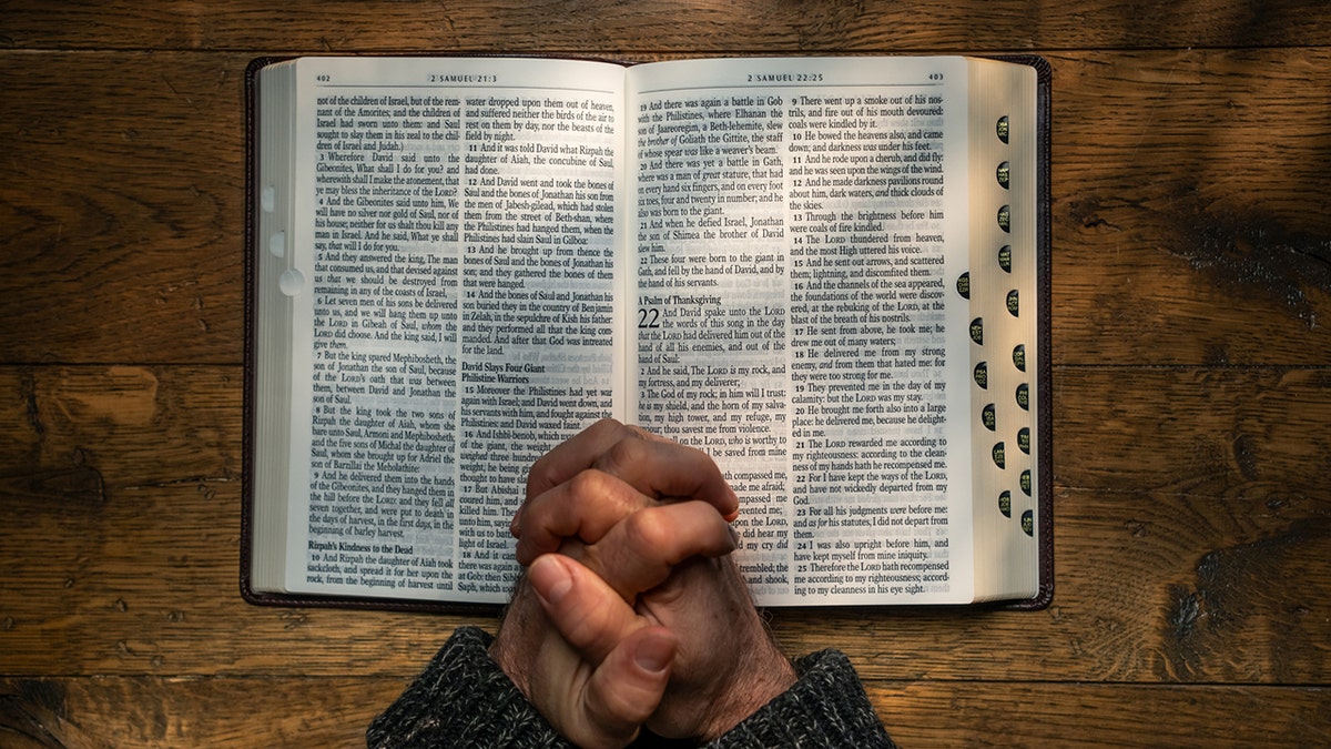 Person with their hands clasped in prayer on the open pages of a Bible.