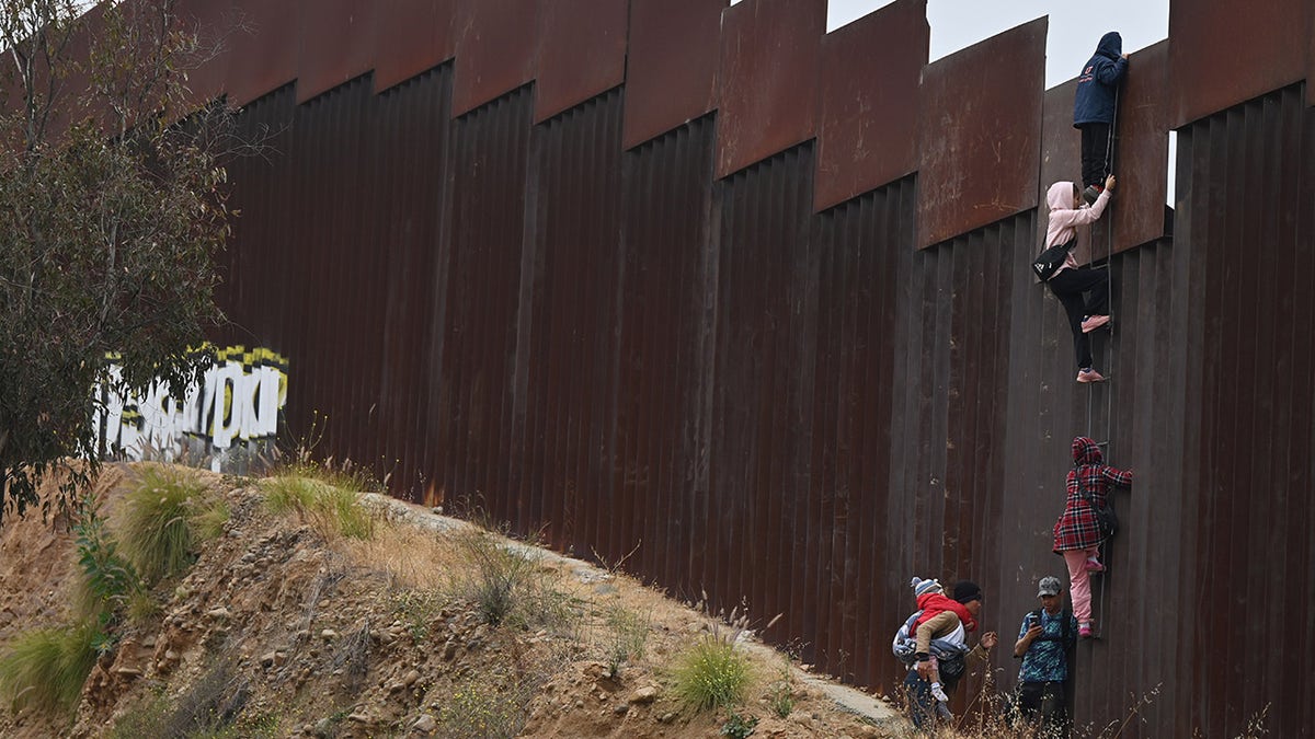 TIJUANA, MEXICO - JUNE 7: A group of adult and child migrants are smuggled at the Tijuana-San Diego border, as they climb the wall to seek asylum in the United States in Tijuana, Baja California, Mexico, on June 7, 2024. 