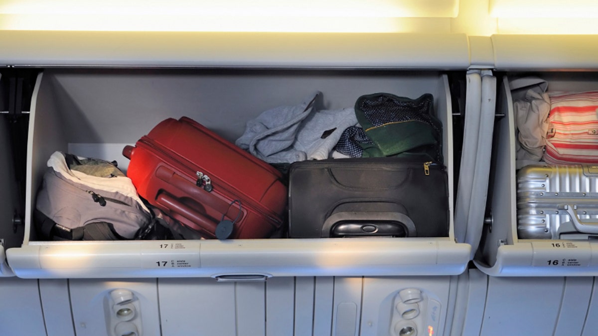 Carry-on luggage in overhead storage compartment on commercial airplane.