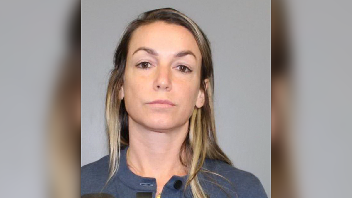 Karen Read in a mugshot standing in front of a gray wall, wearing a blue-gray sweater with buttons