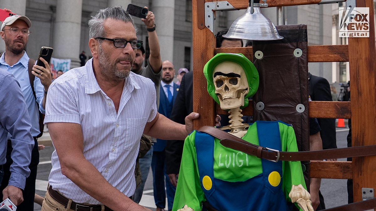 Luigi Mangione faces a potential death penalty as a an artist pushes a sculpture of a skeleton in an electric outside of federal court