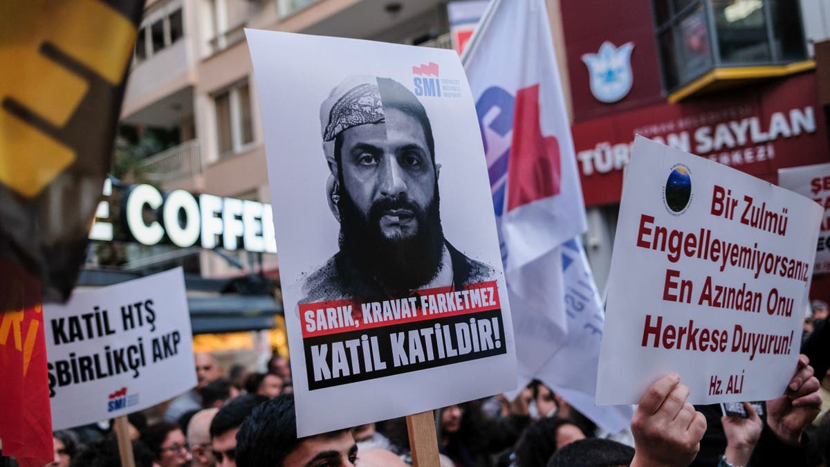 A protester holds a placard with a photo of Ahmed al-Shara (Colani) and the words "It doesn't matter if he wears a turban or a tie, a murderer is a murderer" during the demonstration.