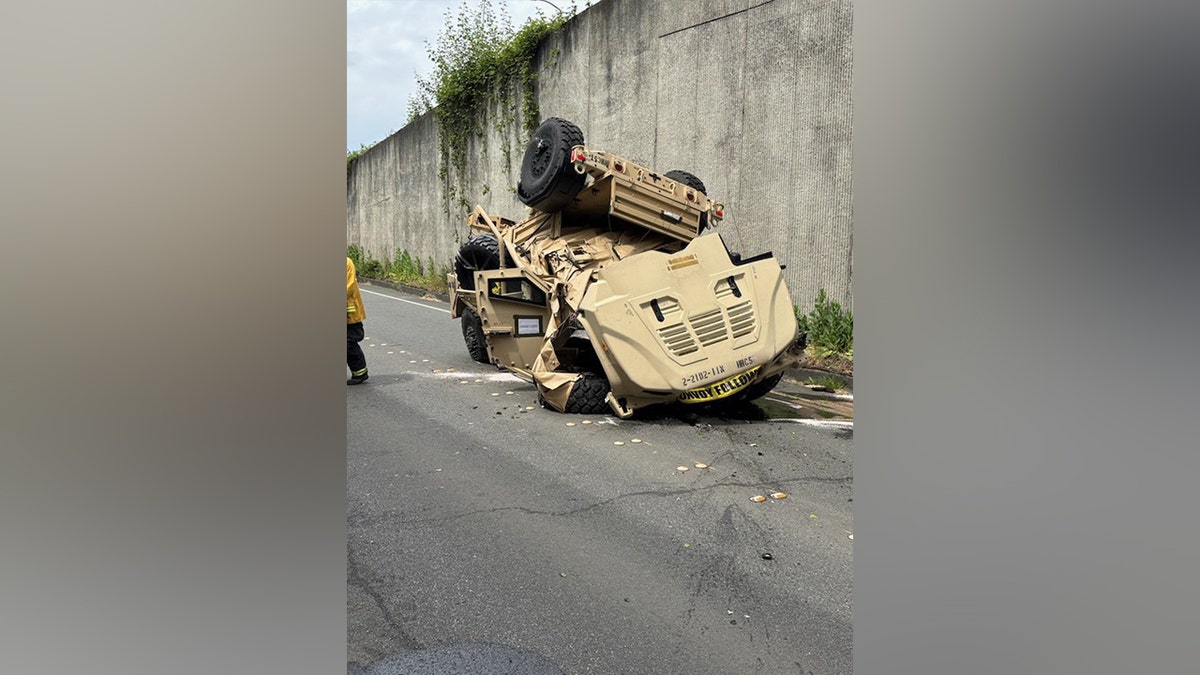 Crash scene showing a military vehicle below an overpass it fell from