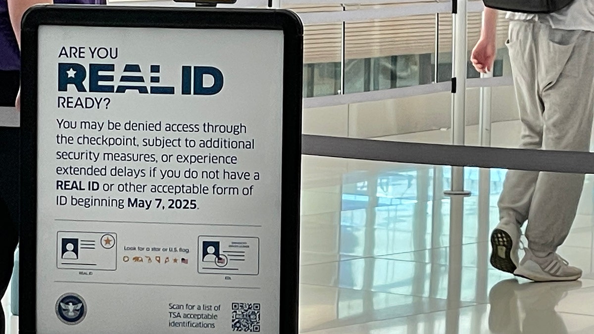 A REALID sign at the Denver airport, a very close shot of a sign about with a person in the background of the shot. The sign reads "Are you REALID ready? You may be denied access through the checkpoint, subject to additional security measures, or experience extended delays if you do not have a REAL ID or other acceptable form of ID beginning May 7, 2025."