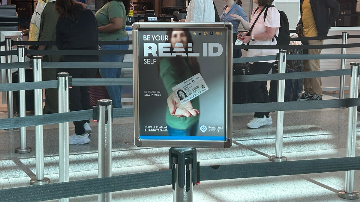 A sign at an airport of a woman holding out her "REAL ID" to encourage travelers to get their REAL ID done before the travel ban takes place.