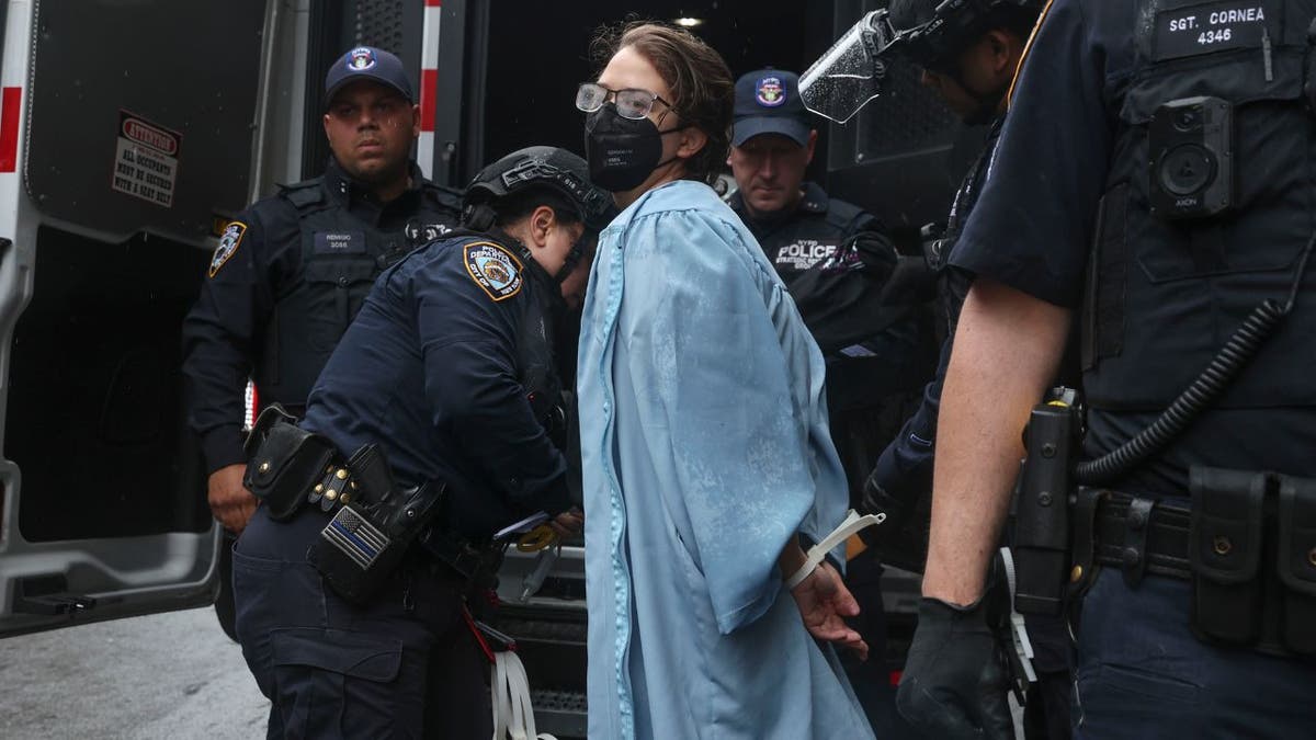 A person wearing graduate robes is detained by police at Columbia University