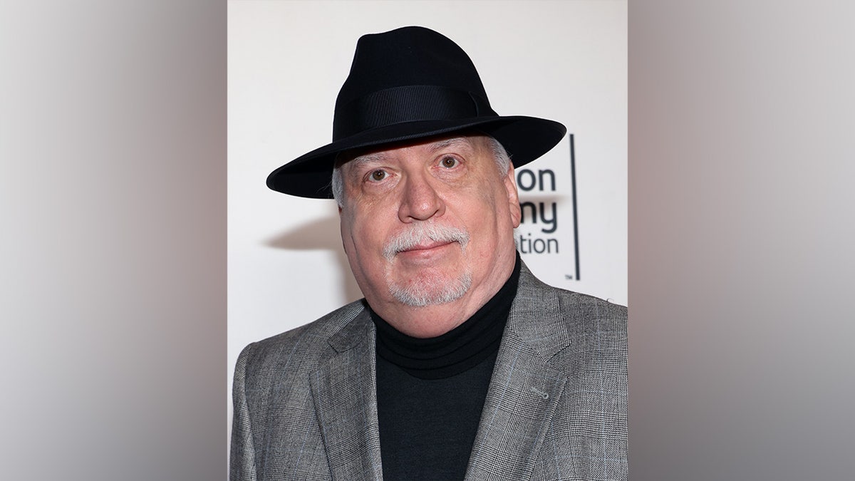 J. Michael Straczynski in a charcoal gray suit, black turtleneck and a black hat