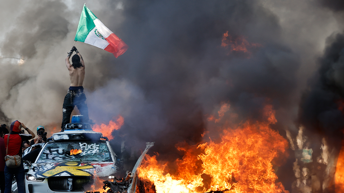 LA rioter waves Mexican flag atop car as fire burns nearby