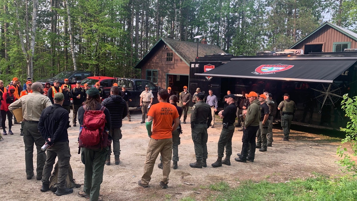 A search party circled up receiving instructions wearing orange and camouflage clothing