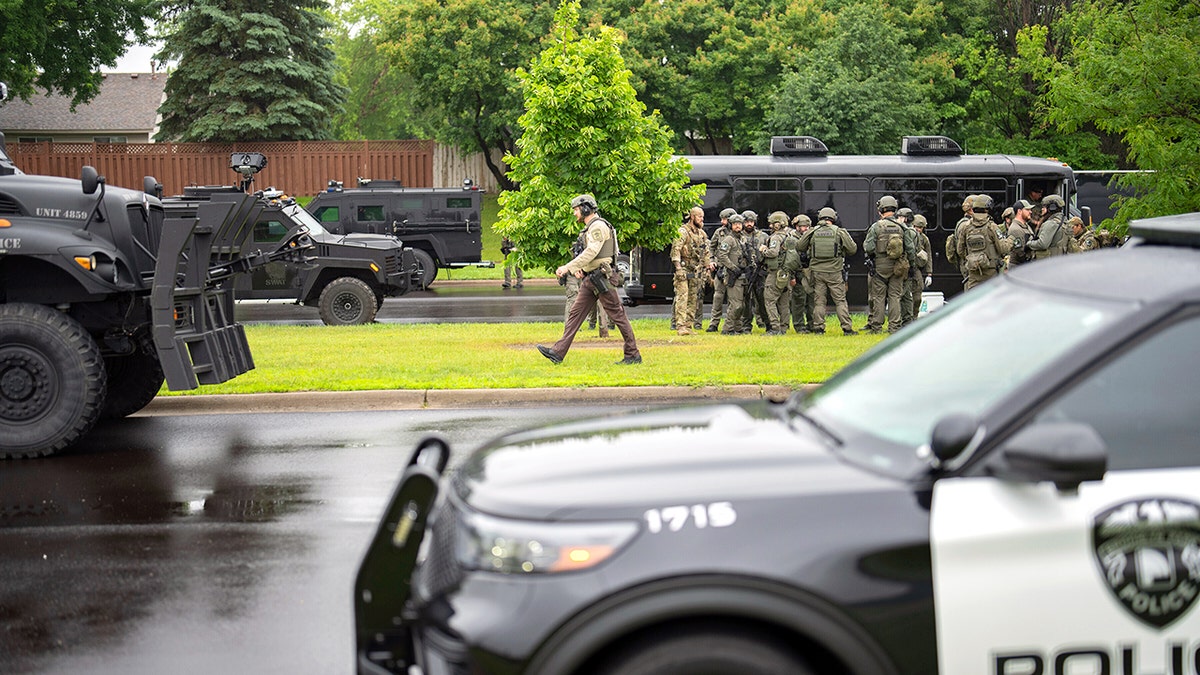 Troops on a lawn in front of houses with a police car in front