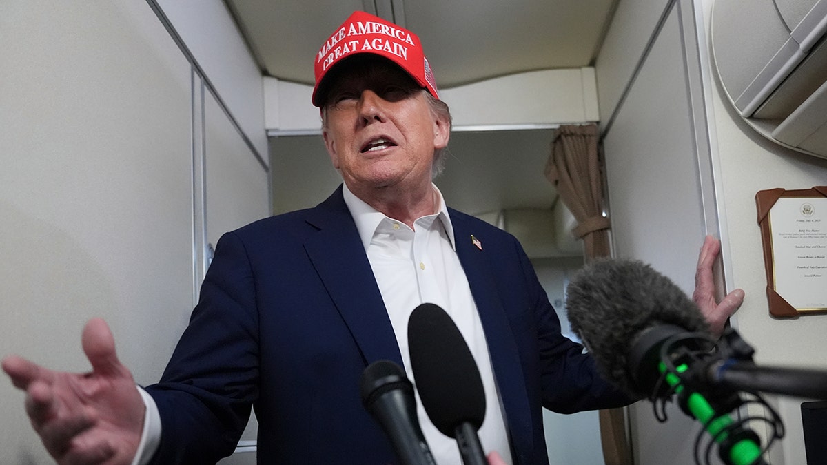 Trump in red MAGA hat talking to reporters on plane