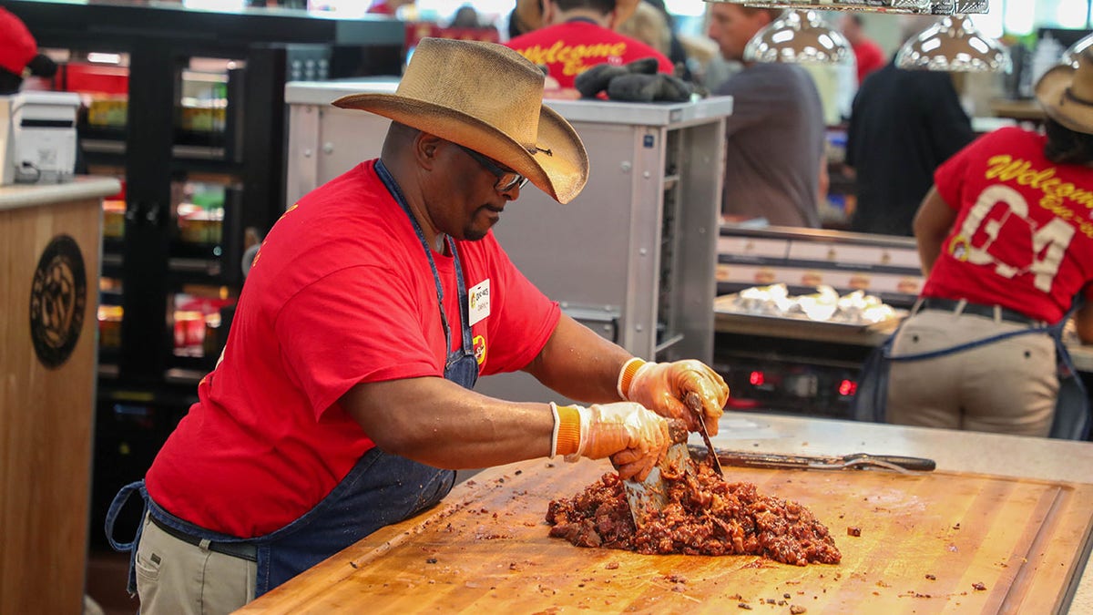 An employee chops up the sauced BBQ during the grand opening of Buc-ee's in Brunswick on Tuesday, July 1, 2025. Seen wearing red shirt and cowboy hat, chopping meat on wood counter.