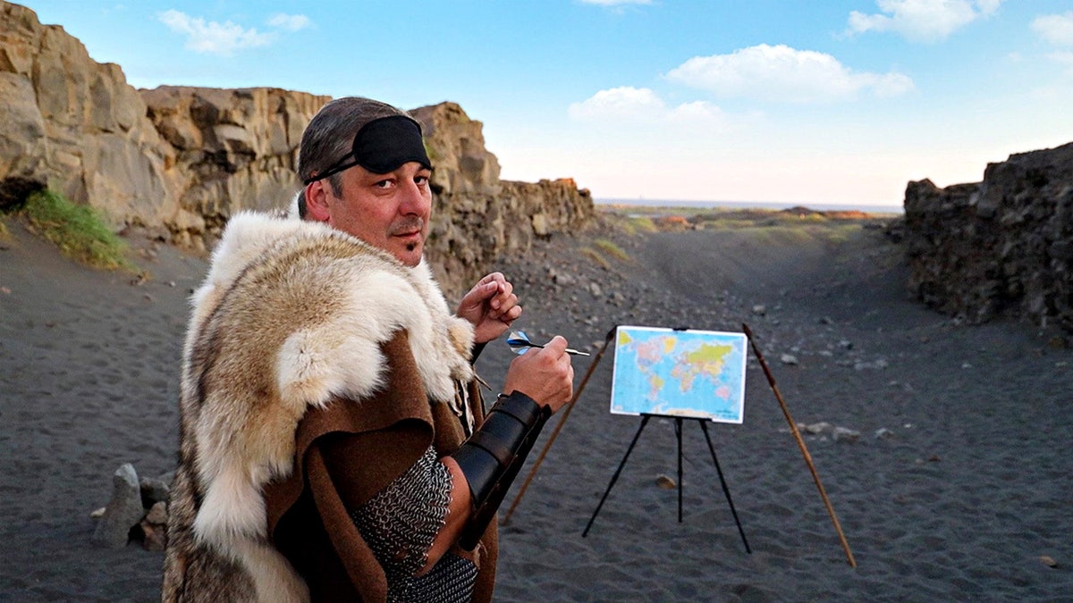 Sorin Mihailovici throwing a dart in Iceland. A man has travelled to over 60 countries by throwing a dart a world map and visiting where ever it lands.
