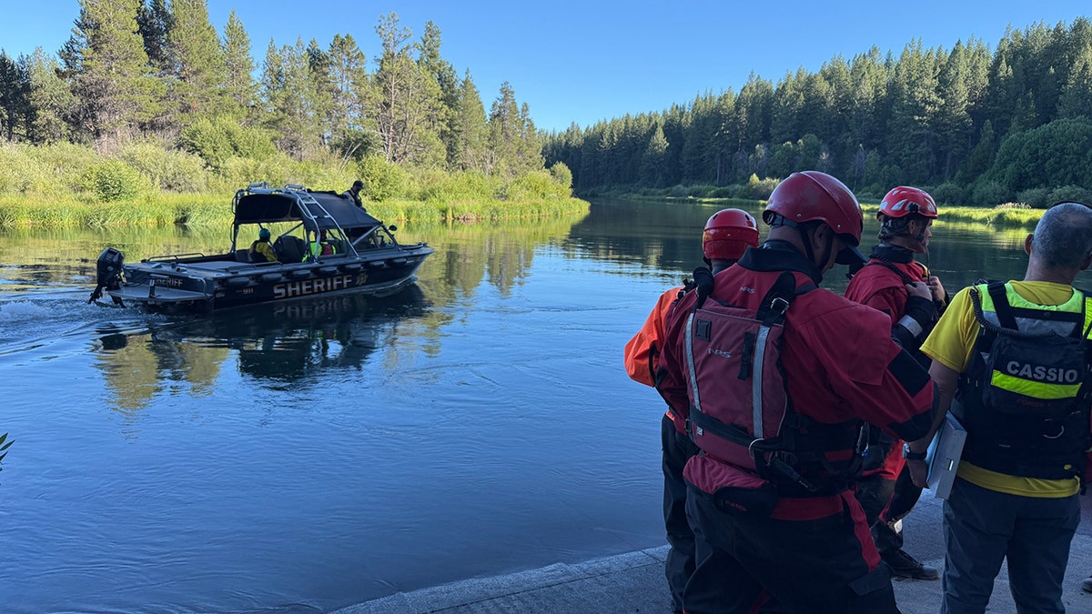 Marine patrol boat on river with team members huddled on the riverbank