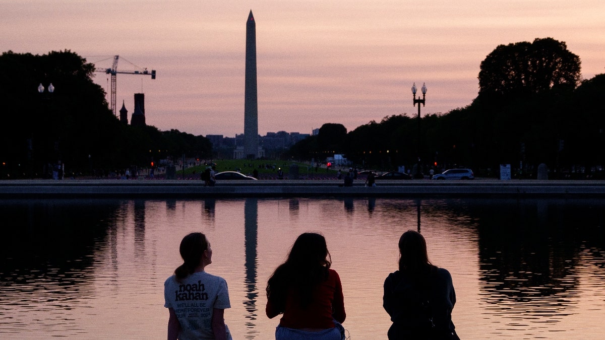 People watch the sunset as the Washington Monument reflects in the Capitol Reflecting Pool on a warm evening on June 2, 2025 in Washington, DC. Smoke from wildfires in Canada have drifted south to make the air the Washington area hazy.