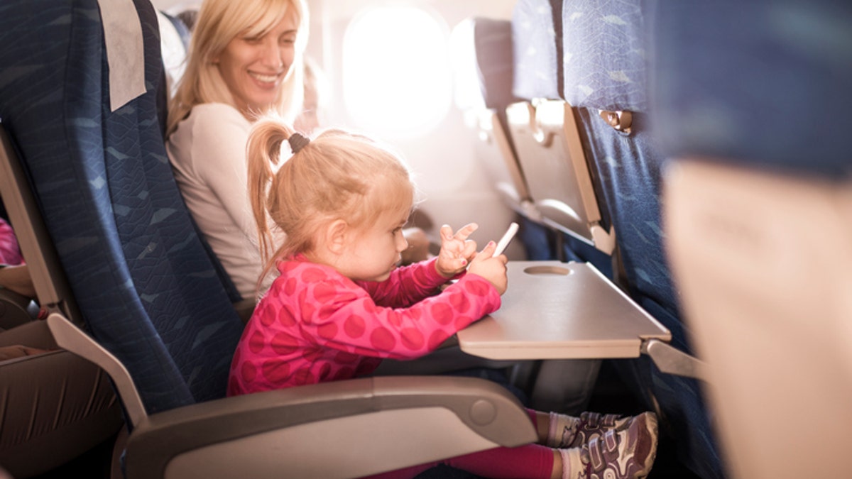 Little girl playing games on cell phone while traveling by plane with her mother. Focus is on little girl.