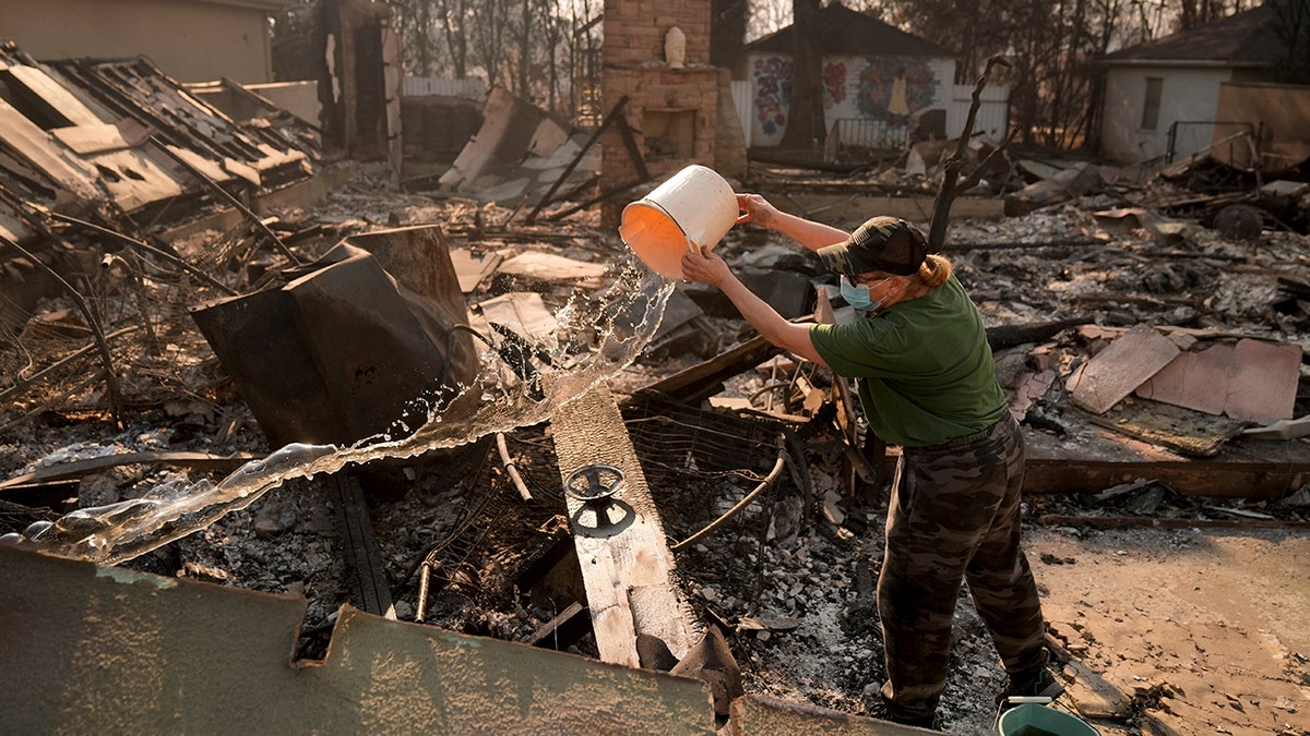 Nancy Belanger pours water on a neighbor's fire-ravaged property in the aftermath of the Palisades Fire in the Pacific Palisades neighborhood of Los Angeles, on Thursday, Jan. 9.
