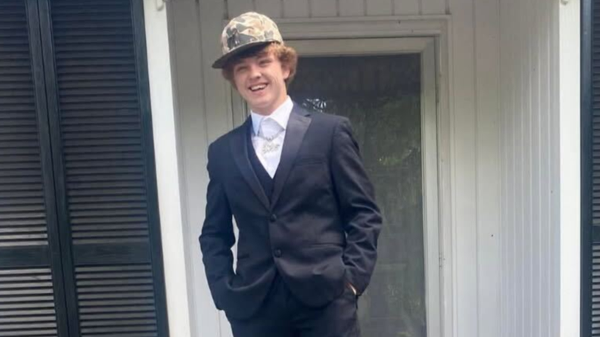 Trey Wright dressed up in formal attire - plus a hunting hat - for a school dance as he smiles on a porch