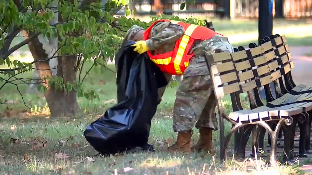 Guard member bends to pick up litter near benches in Lafayette Park