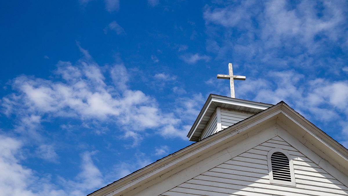 A wooden cross crowns the roof of a traditional white church