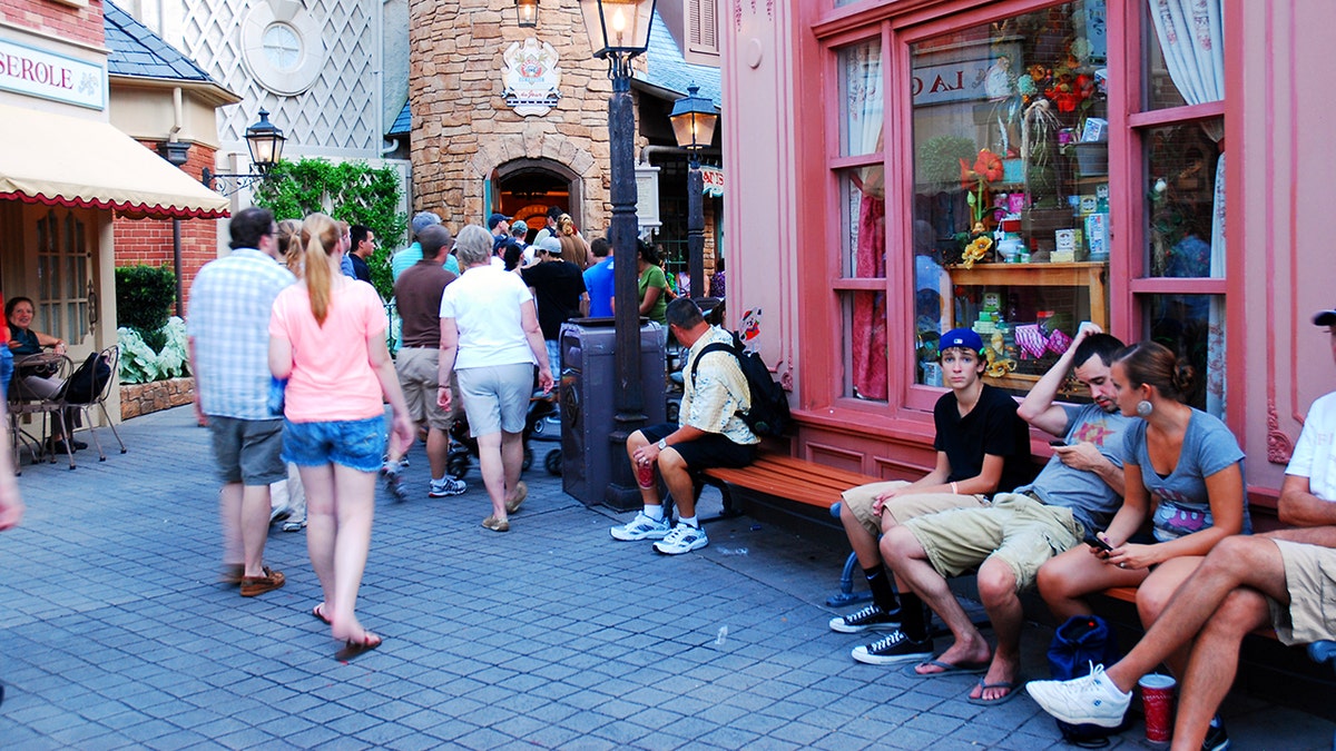 Adults sitting around outside French-themed shops at Walt Disney World park