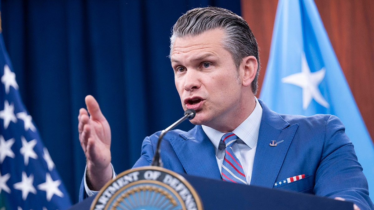 Defense Secretary Pete Hegseth wearing a blue suit and gesturing with his hand during a Pentagon briefing