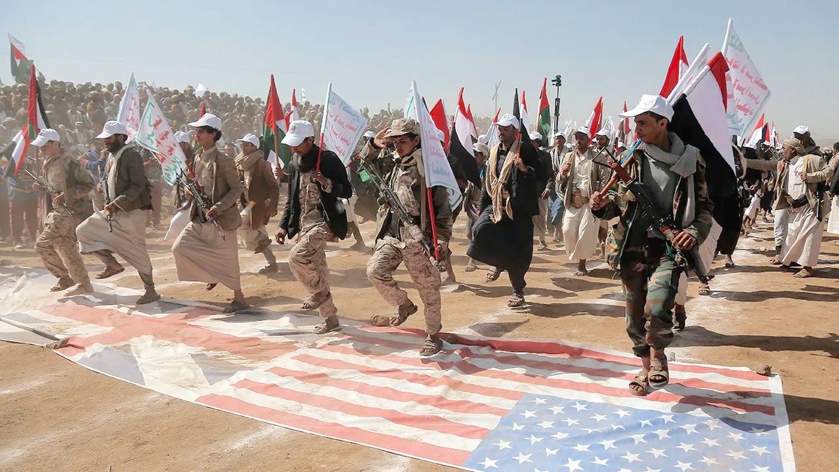 Houthi fighters march over U.S. and British flags at a rally in Yemen.