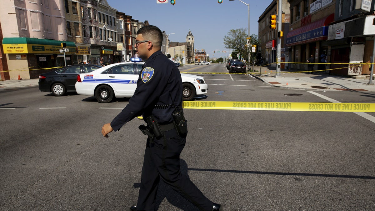 A Baltimore police officer attempts to secure a crime scene with tape at the scene of a shooting at the intersection of West North Avenue and Druid Hill Avenue in West Baltimore, Maryland May 30, 2015. Local media have reported more than 35 murders in the city of Baltimore since the April rioting over the death of 25-year-old resident Freddie Gray and shootings continue regularly in his West Baltimore neighborhood. REUTERS/Jim Bourg - RTR4Y6G0