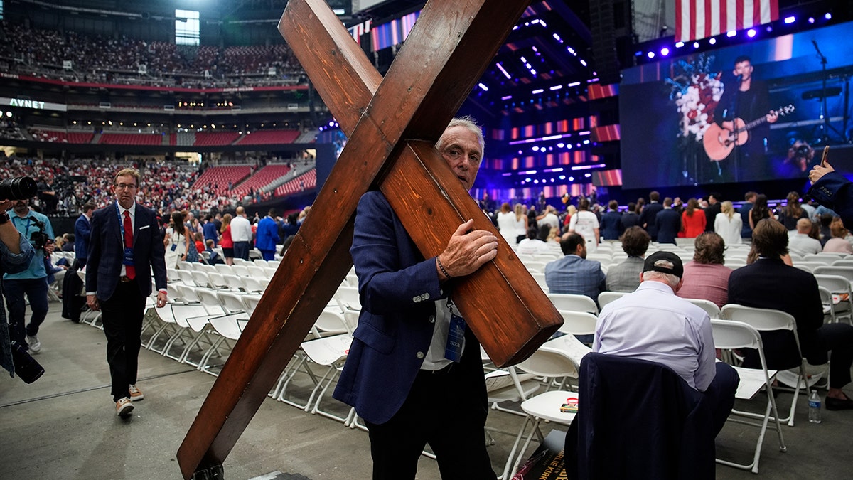 Dan Beazley carries a cross at a memorial for conservative activist Charlie Kirk, Sept. 21, 2025, at State Farm Stadium in Glendale, Arizona.