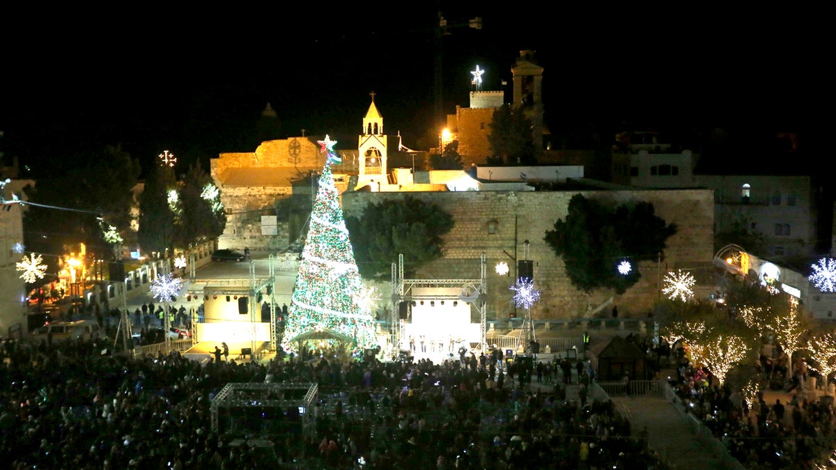 People attend the lighting of a Christmas tree in Manger Square, outside the Church of the Nativity in the West Bank town of Bethlehem at night