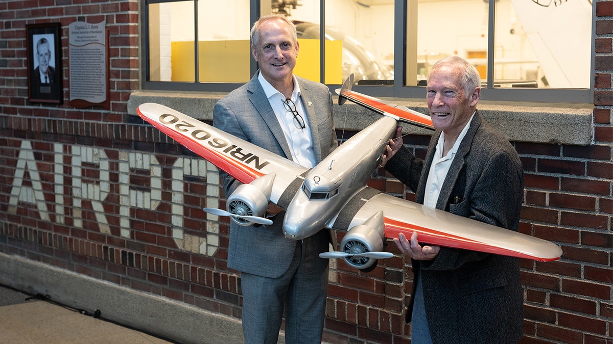 Two men holding up model of airplane