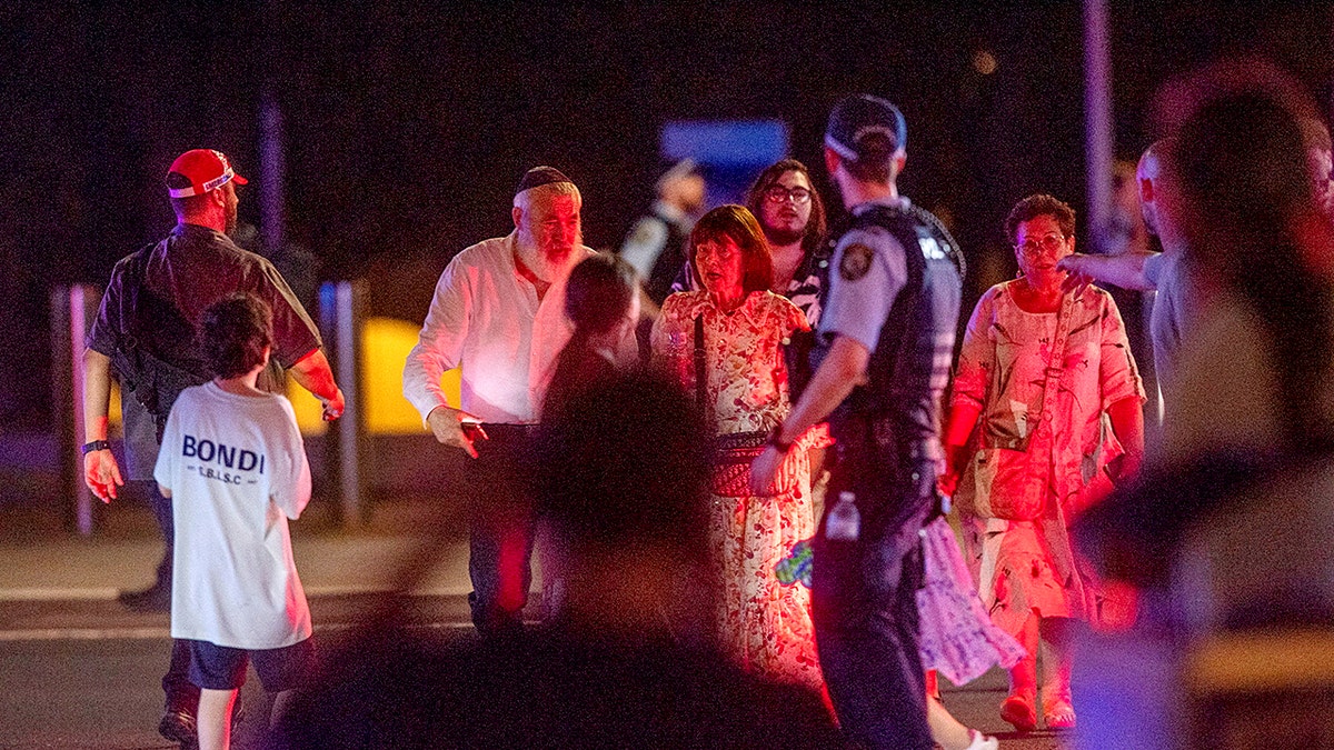 People walk as police officers stand guard on the street following a shooting incident at Bondi Beach, in Sydney, Australia, Dec. 14, 2025. 