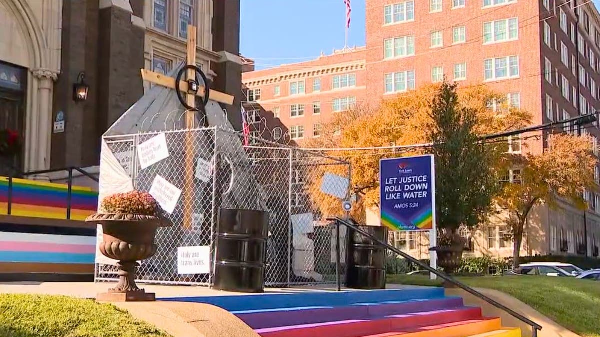 Outdoor nativity behind a chain-link fence on rainbow-painted church steps.