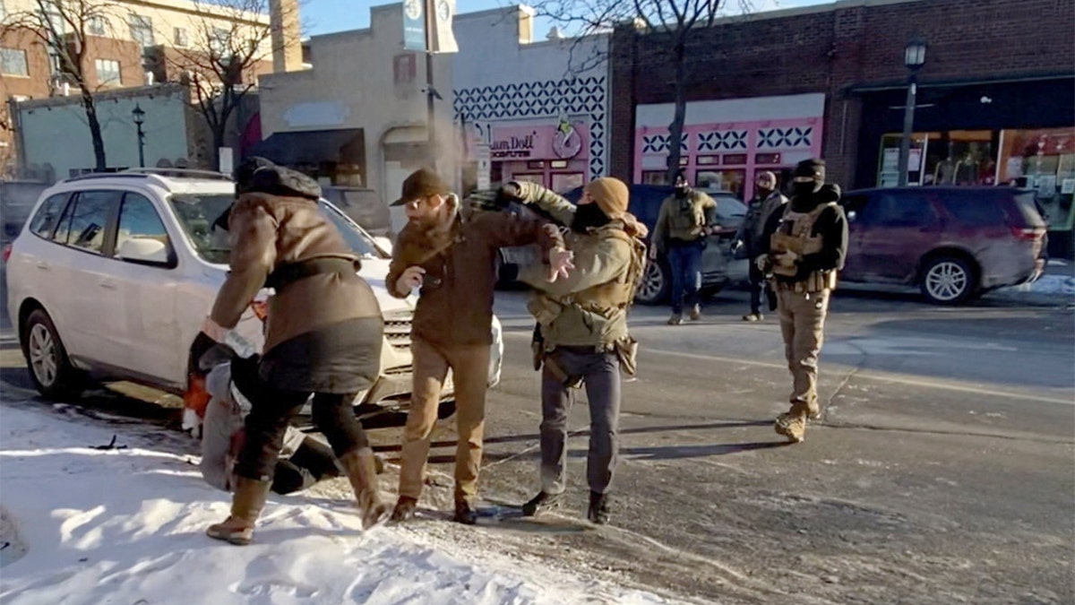 A law enforcement officer deploys a chemical spray toward a man during a confrontation on a city street.