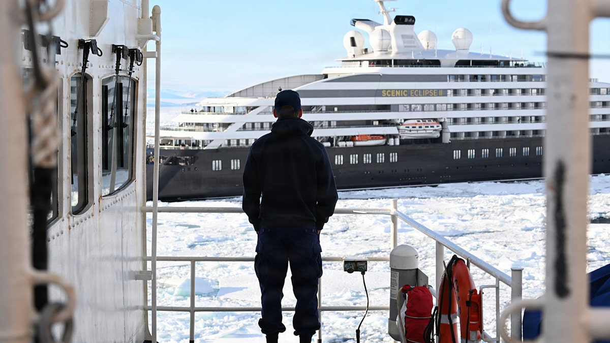 Crew member standing on ship deck watching Scenic Eclipse II cruise ship in icy polar waters