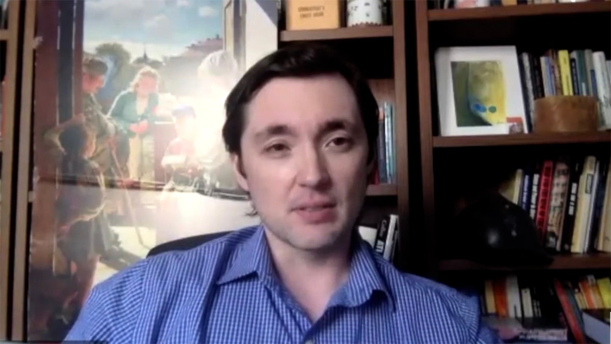 University of Toronto professor speaks online with bookcase in background