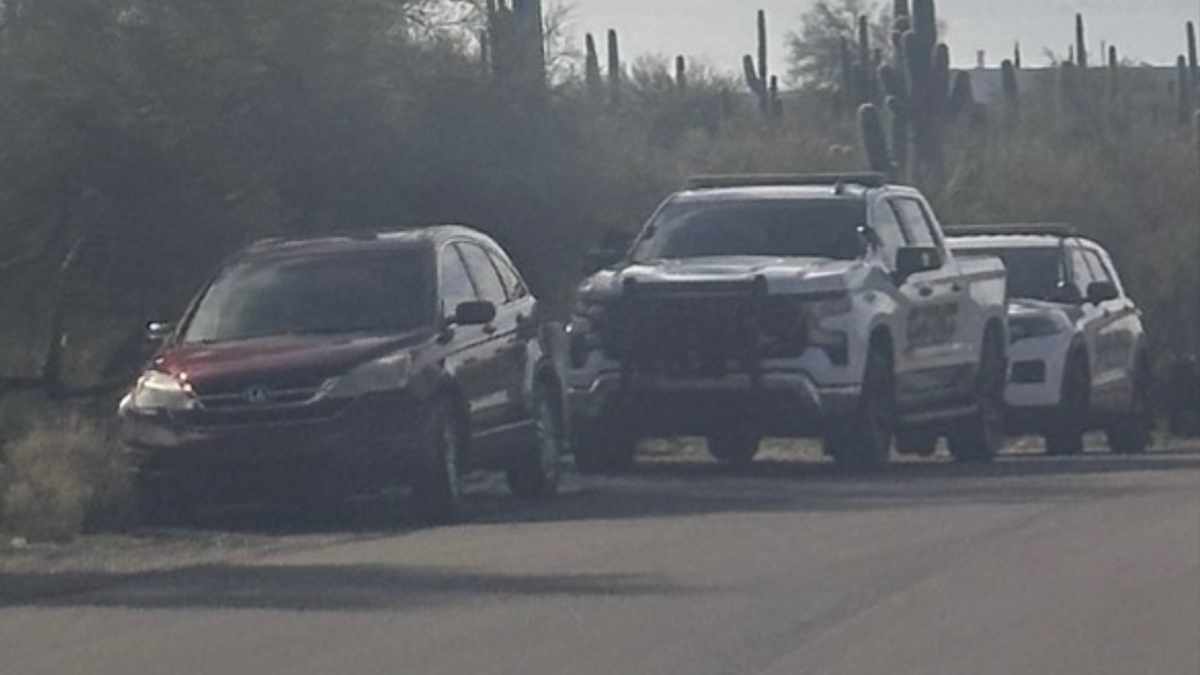 A red Honda SUV and two Pima County Sheriff's Department vehicles parked.