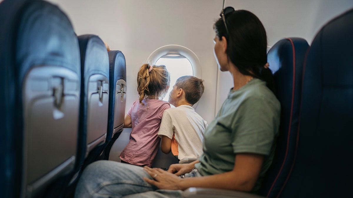 Mother and two children looking out airplane window while seated on a commercial flight.
