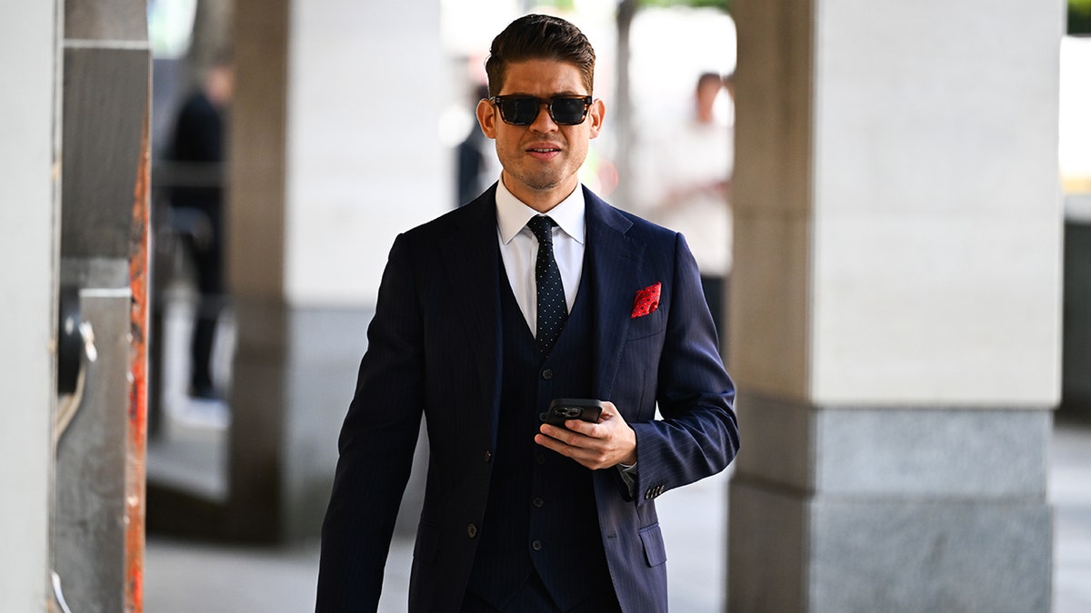Jose Alejandro Zamora Yrala wearing suit, sunglasses and holding a phone while walking