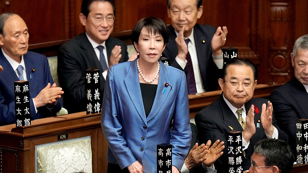 Sanae Takaichi stands as lawmakers applaud.