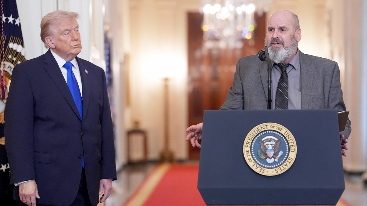 A man speaks beside President Donald Trump in the East Room of the White House.