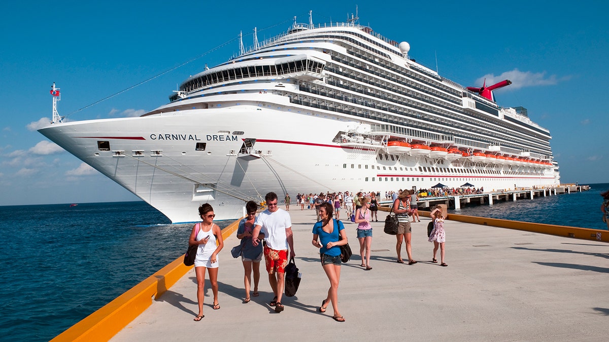 Passengers walk along a pier beside the Carnival Dream cruise ship docked at a tropical port.