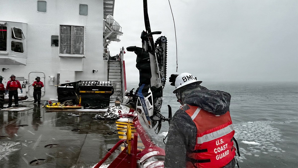 A U.S. Coast Guard crew member lifts a snowmobile from icy waters near Mackinac Island during a recovery operation.