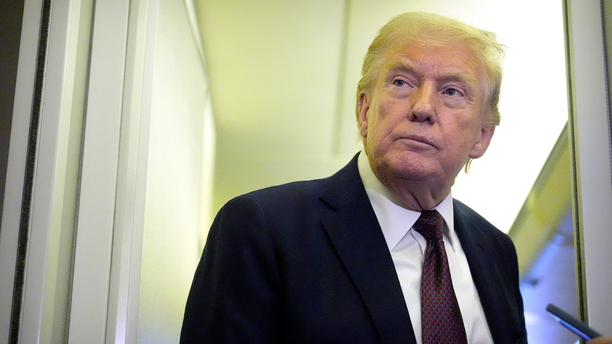 President Donald Trump answers questions from reporters while standing in the aisle of Air Force One during a flight to Maryland.