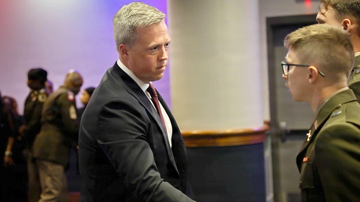 Man in a suit shakes hands with a service member.