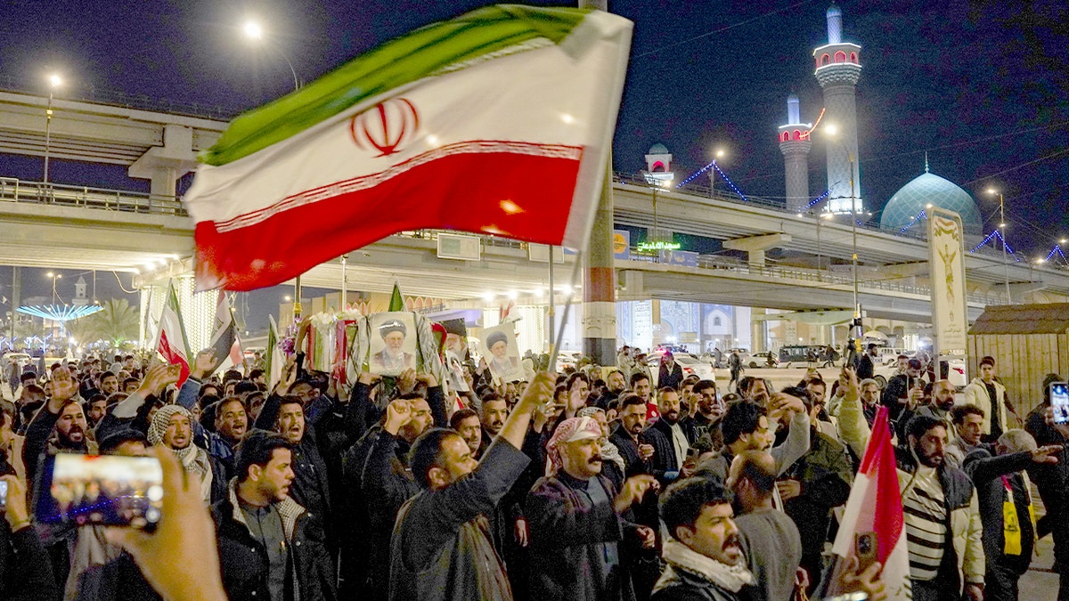 Hundreds of demonstrators march through Najaf waving Iranian flags and holding portraits during a protest.