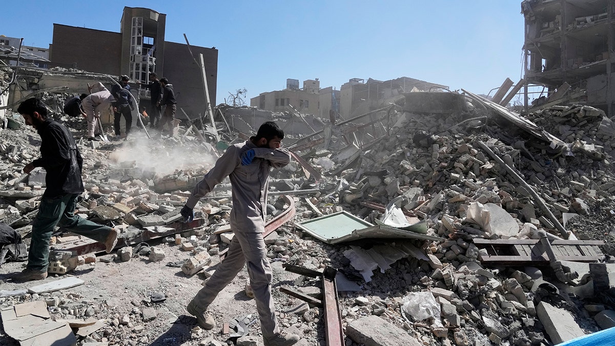A group of men standing and looking at the rubble of a destroyed building.