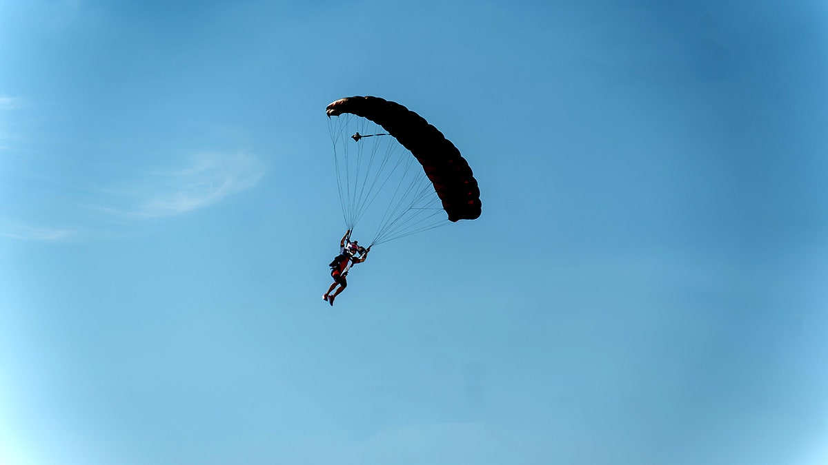 Skydiver descending under a parachute against a clear blue sky during a daytime jump.