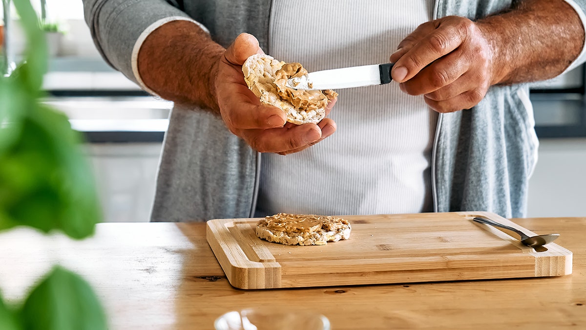 Man making healthy snack by spreading peanut butter on a puffed rice cakes.